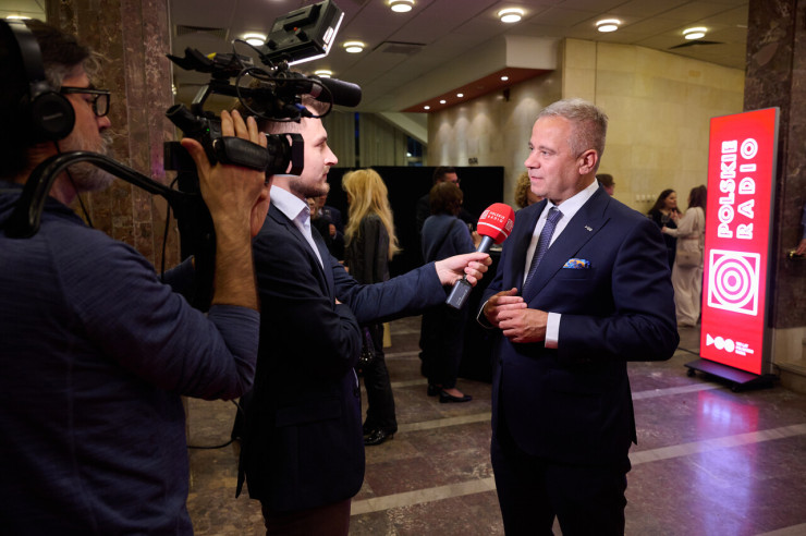 Prezes Polskiego Radia Paweł Majcher mówi do mikrofonu przed kamerą. 