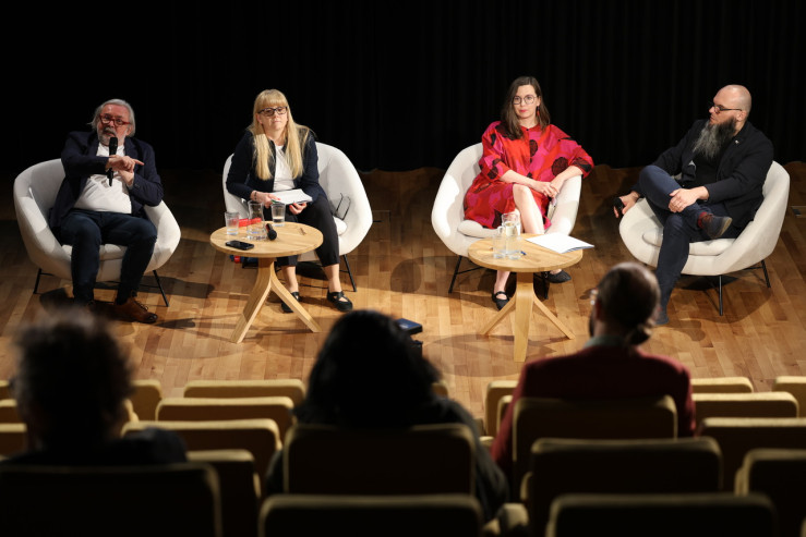Czterech panelistów na scenie siedzi w fotelach. 