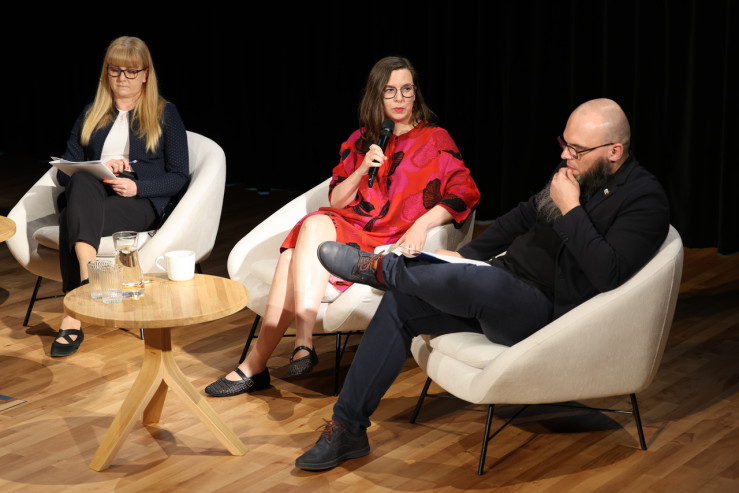 Czterech panelistów na scenie siedzi w fotelach. 