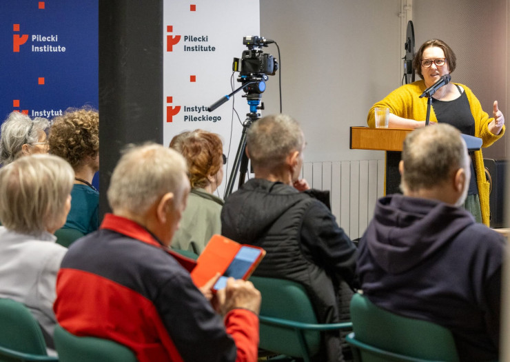 Aleksandra Kaiper-Miszułowicz  przy pulpicie, przed nią publiczność spotkania. 