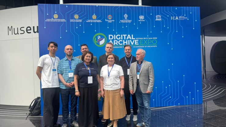 Osiem osób na stojąco pozuje do zdjęcia na tle ekranu z wyświetlonym napisem digital archive