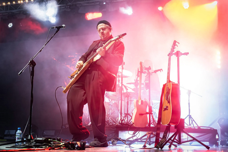 Mężczyzna gra na gitarze na scenie, w tle ekran z animacjami