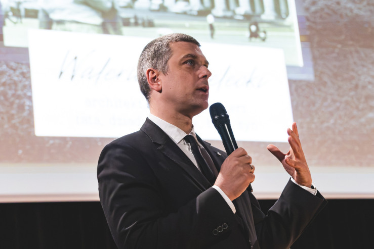 Dyrektor Madaj przemawia do mikrofonu do gości wernisażu. 