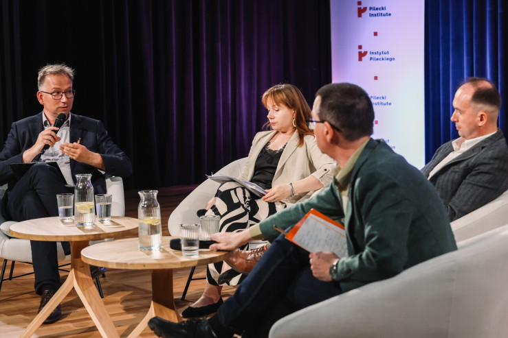 Panel dyskusyjny z udziałem czterech osób siedzących w białych fotelach na scenie Instytutu Pileckiego.  