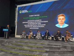 scena konferencyjna na której siedzi w fotelach 5 panelistów, po lewej stronie przy pulpicie do mikrofonu mówi kobieta, z tyłu wielki ekran ok  4 na 7 metrów. 
